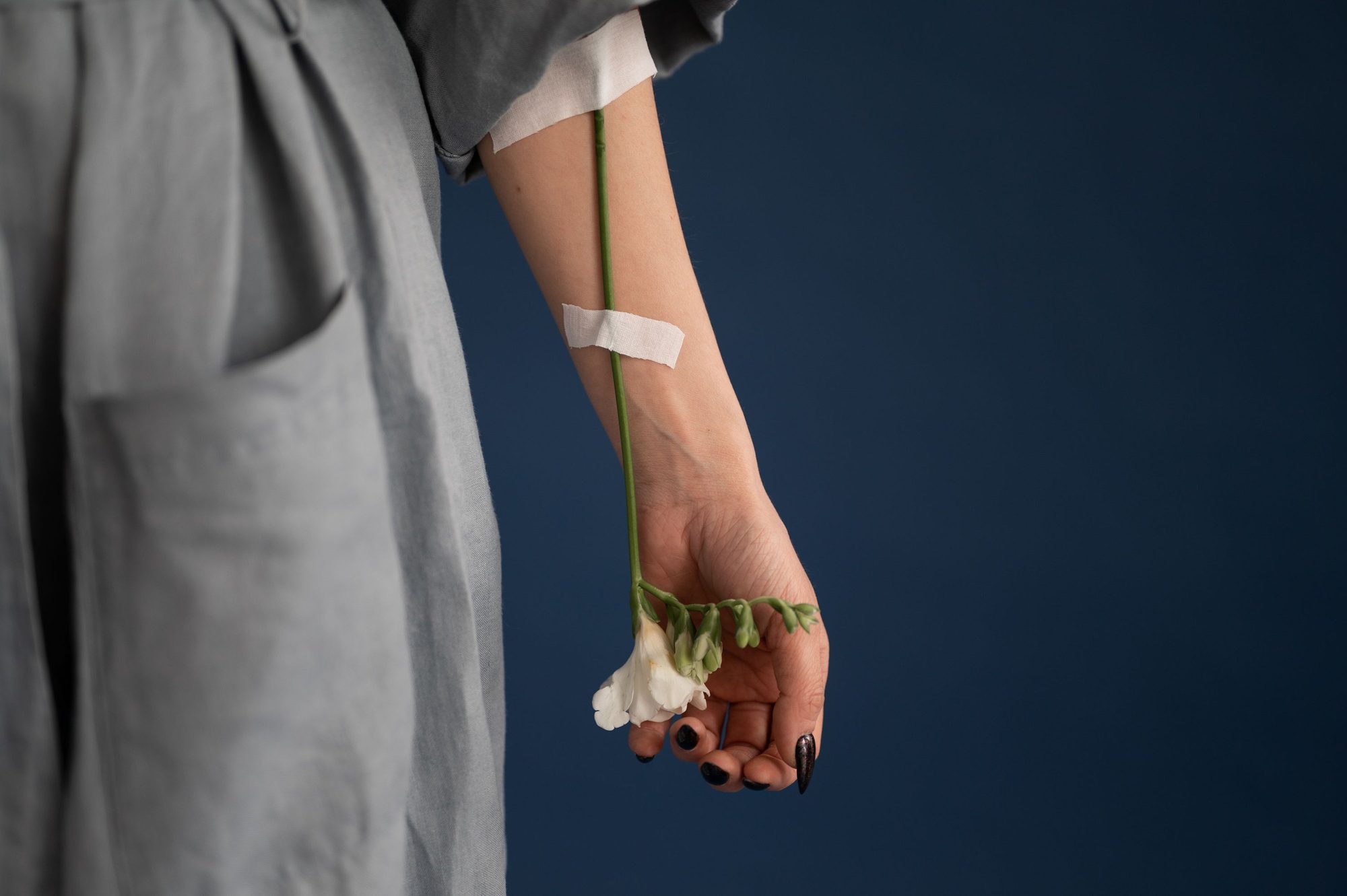 A flower stem taped to a forearm like an IV line, with a white freesia in the hand