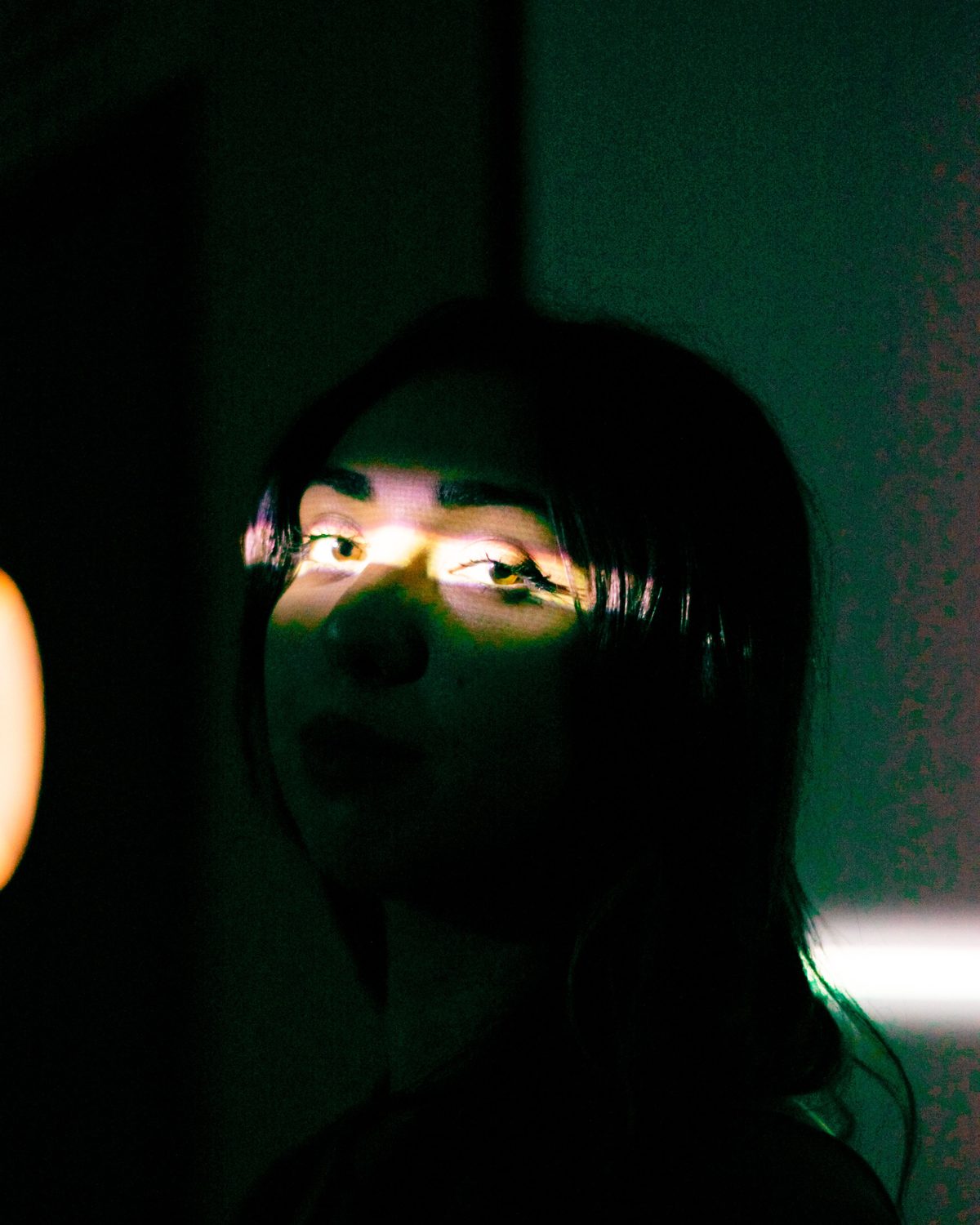 Woman with a band of light across her eyes against a dark teal background